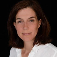 Professional headshot of Christine Leopold, a woman with shoulder-length dark brown hair wearing a white top, against a dark background.