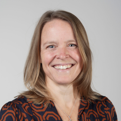 Professional headshot of Mira Zuidgeest, a smiling woman with shoulder-length light brown hair wearing a patterned navy and orange top, against a plain background.