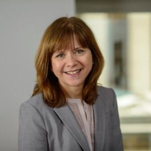 Professional headshot of Susan Oliveria, a smiling woman with shoulder-length auburn hair wearing a grey blazer, against a blurred background.