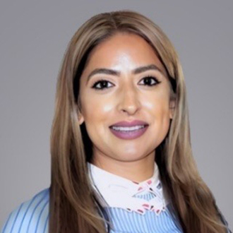 Professional headshot of Mariam Bibi, a smiling woman with long brown hair wearing a light blue top over a floral blouse, against a plain background.